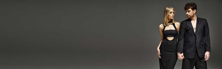 elegant couple in black attire holding hands on grey backdrop, handsome man and blonde woman, banner