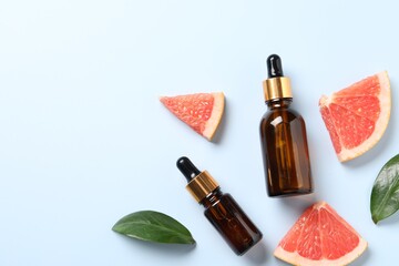 Grapefruit essential oil in bottles, leaves and cut fruit on light blue table, flat lay. Space for...
