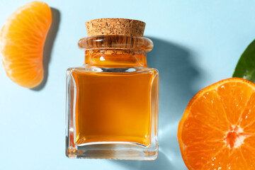 Aromatic tangerine essential oil in bottle and citrus fruit on light blue table, top view