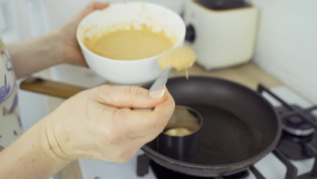A woman bakes pumpkin cheesecakes in a frying pan using a mold. Place the apple, pumpkin and cinnamon batter into the mold. Close-up.