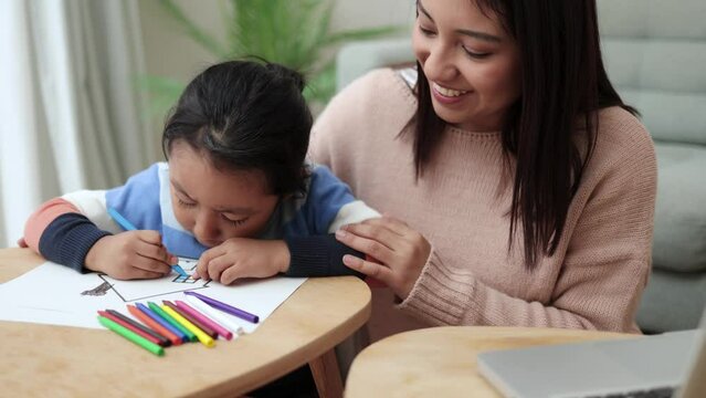 Asian mother taking care of her child painting while using computer laptop at home. Family lifes tyle