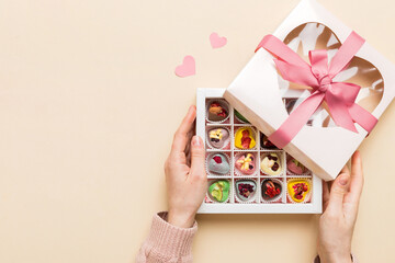 Female hands with delicious candies in box on color background