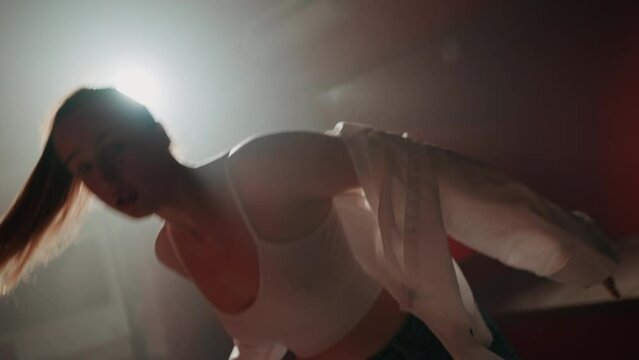 Young attractive woman is dancing hip hop contemporary in dace hall close-up on white light. Shooting of modern slow dance choreography. Motion of female dancer expressing feelings in dance movings. 