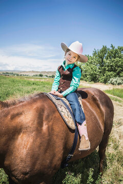 Young cowgirl on her horse, wearing cowboy hat and boots. Bridger, Montana, USA