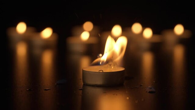Burning candles. The candles burn against a black background and the flames move when the wind blows. The concept of a memorial day. Background for advertising and design projects.
