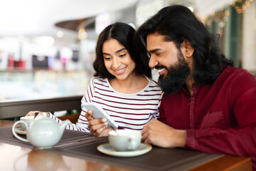 Beautiful indian couple with smartphone on date in coffee shop