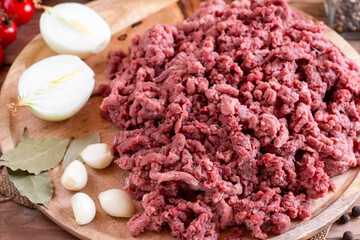 Fresh minced beef on cutting board on table with ingredients for cooking, top view