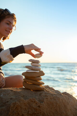 beautiful adult girl on the ocean shore builds a tower of stones, balancing and enjoying the process. © Anna