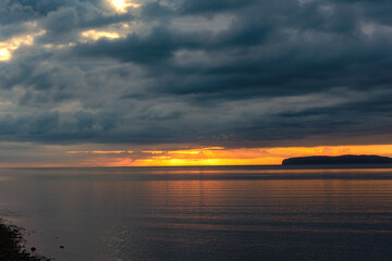 Obraz premium Bright orange sunrise on the coast with dark dramatic clouds with wind farm turbines far in the distance. Beaumaris, North Wales