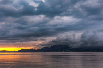 Bright orange sunrise on the coast with dark dramatic clouds billowing over mountains in the distance. Beaumaris, North Wales