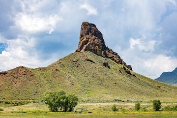 Fototapeta na wymiar Castle Rock formation, hill and trees landscape with cloudy blue sky in the wilderness of northwest Wyoming near Cody, USA. 