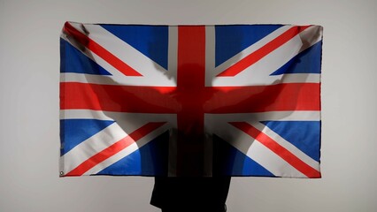 Person silhouette holding big flag against white background. Silhouette of man with national flag of Great Britain holding in hands.