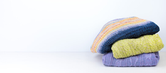 Knitted woolen sweaters. A bunch of knitted winter, autumn clothing on a white background, sweaters, knitwear, space for the text. Banner.