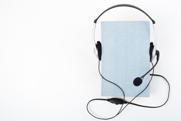 Audiobook on white background. Headphones put over blue hardback book, empty cover, copy space for...