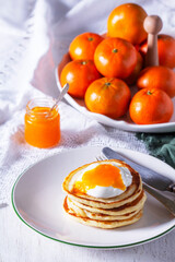Pancakes served with tangerine jam and sour cream, and tangerines on a light background.
