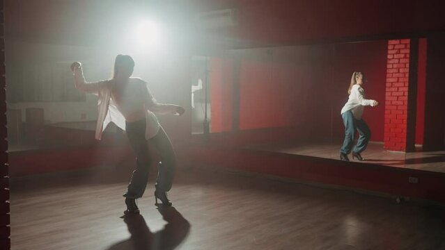 Young attractive woman is dancing hip hop contemporary in dace hall close-up on white light. Shooting of modern slow dance choreography. Motion of female dancer expressing feelings in dance movings. 