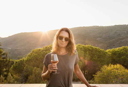 Woman standing in the evening sun drinking champagne with Italian landscape in the background. Elba Island, Italy