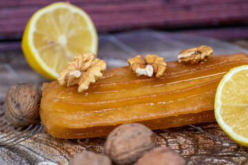 Turkish sweet cake called tulumba, served at plate with sliced of lemon and nuts around, on massive wooden table