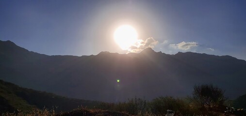 A distinctive view of the setting sun behind the mountains and trees