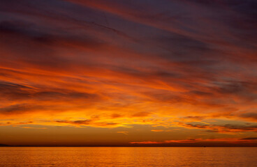 Naklejka na ściany i meble Sunset over the sea. Bright orange and red clouds. Dramatic sky
