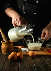 A chef prepares a milkshake with fruits in the kitchen using a hand-held electric mixer. The cook...