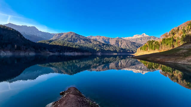 Scenic view of alpine lake Sauris (Lago di Sauris) in Friuli Venezia Giulia, Italy. Looking at water reflection of majestic mountain ridges of Carnic Alps. Serene tranquil atmosphere in Italian Alps