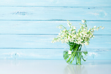 Bouquet of lilies of valley in transparent vase on  blue wooden wall background.