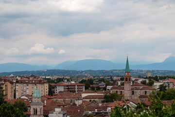 Fototapeta na wymiar Aerial panoramic view of historic city of Udine, Friuli Venezia Giulia, Italy, Europe. Viewing platform form castle of Udine. Cloudy overcast day. Distant view of mountains of Alps, border to Austria