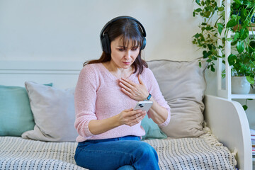 Middle aged woman in headphones using smartphone for video call, conference