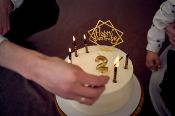 father lights candles on his son's second birthday cake - obrazy, fototapety, plakaty