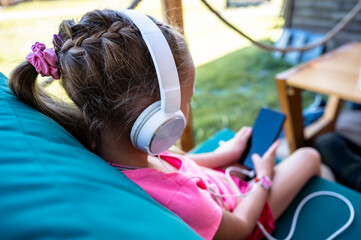 Toddler girl sitting in cafe with headphones and mobile phone in her hands playing games