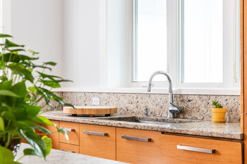 Detail shot of a sink in a luxury kitchen with a chrome faucet, light wood cabinets, and granite...