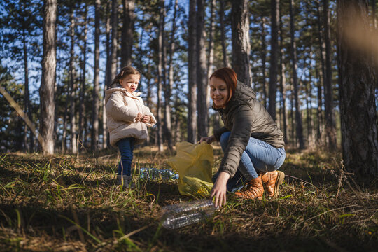 mother and daughter collect plastic bottle garbage waste in forest