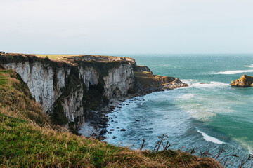 Fototapeta na wymiar A stunning backdrop of cliffs on a cloudy day in Northern Ireland, where the vibrant blue waves crash against the rocky shore