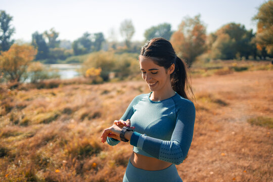 A smiling athletic young woman checking pulse on her smart watch after her outdoor jog
