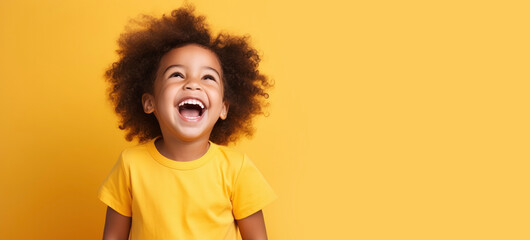 Laughing happy african american kids child todler wearing a yellow t-shirt on yellow background. Dark-skinned child smiles, rejoices, portrait. Preschool education concept, kindergarten