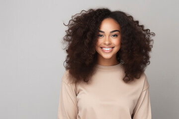 Beautiful young African American woman with curly hair smiling in light clothes against a light background. Happy girl, human emotions