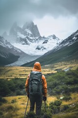 Fototapeta na wymiar A hiker in orange jacket gazes at snowy mountains amidst greenery under a cloudy sky.