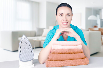 beautiful young woman leaning on an ironing board with an iron looks at the camera and smiles while ironing clothes at home in the living room. Blurred background Home interior. Soft focus.
