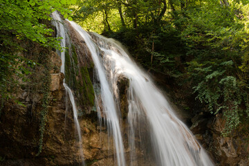 A beautiful landscape of a small deep waterfall with flowing water on the European mountain river.