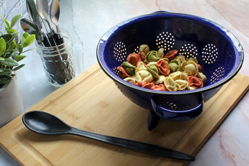 Tri-colored fresh tortellini pasta in a colander, ready to cook
