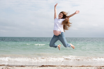 Obraz premium A happy pregnant woman jumps in the air. Happy pregnancy. Active, healthy pregnancy. A pregnant woman near the ocean jumping with glee