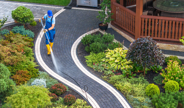 Homeowner Cleaning Backyard Garden Brick Paths Using Pressure Washer
