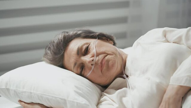 Close-up of an elderly woman lying with a nasal cannula in bed, weakened health