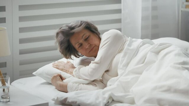 Distressed senior woman finds no rest on an uncomfortable pillow, insomnia