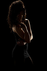 Enigmatic Elegance: Curly-Haired Woman's Silhouette On A Dark Studio Background.