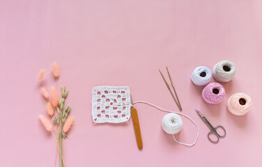 Top view of crocheting process of white square lace doily on pink pastel background. Skeins of yarn for knitting, crochet hooks and bouquet of ears of oats and lagurus nearby. Copy space, flat lay - obrazy, fototapety, plakaty