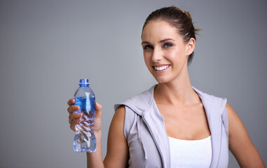 Happy woman, portrait and water bottle in fitness for hydration on a gray studio background. Face...