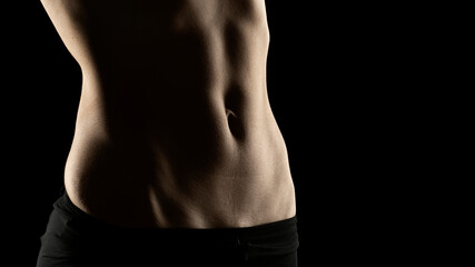 Close-up of a fit woman's stomach under the glow of light in a dark background - obrazy, fototapety, plakaty