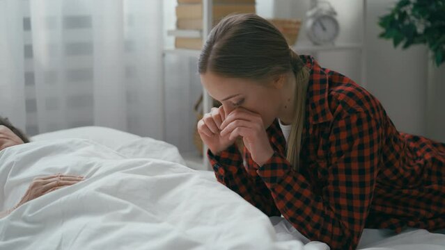 Young woman grieving by critically ill grandmother's bedside, hope for recovery
